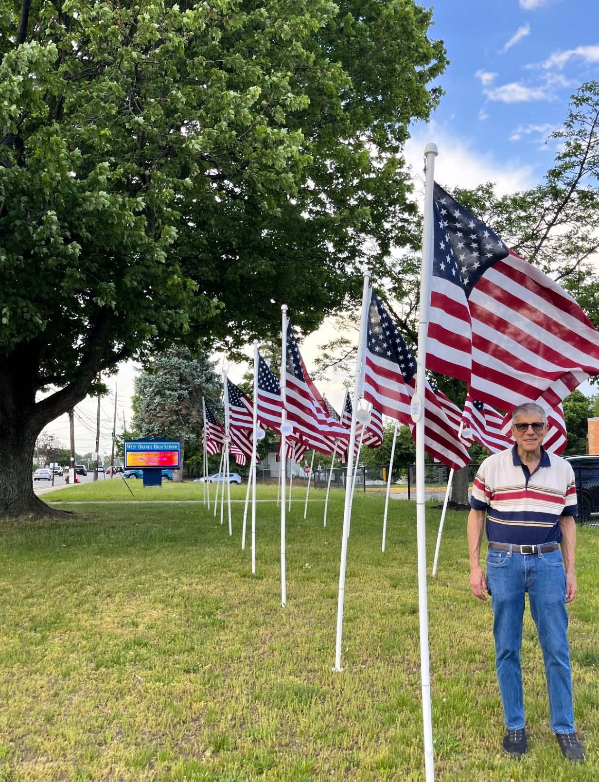 Larry Poster standing among a line of American flags at West Orange High School